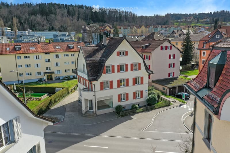 Aerial view of a residential area with multiple houses, red-tiled roofs, and surrounding greenery.