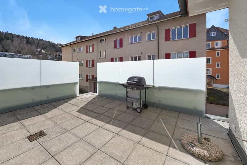 Modern outdoor patio with tiled flooring, white privacy screens, and a grill in the center.