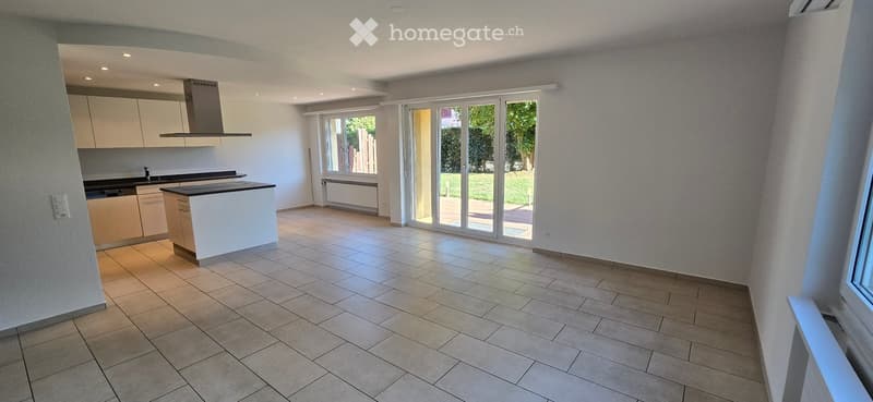 Empty kitchen with tiled floor, white cabinets, island, and large sliding glass doors leading to a garden view.