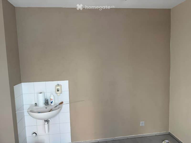 Small bathroom with a white sink, tiled wall, and a soap dispenser. The walls are painted in a light beige color, and the floor is tiled.