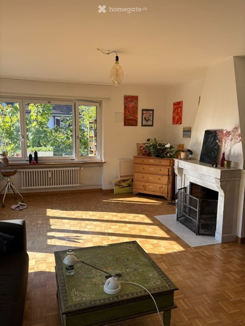 Bright living room with wooden flooring, large windows, fireplace, sofa, coffee table, and decorative items.