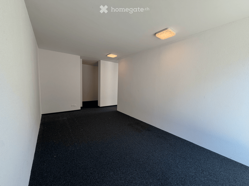 Empty room with white walls, black carpeted floor, and recessed lighting. No furniture or equipment present.