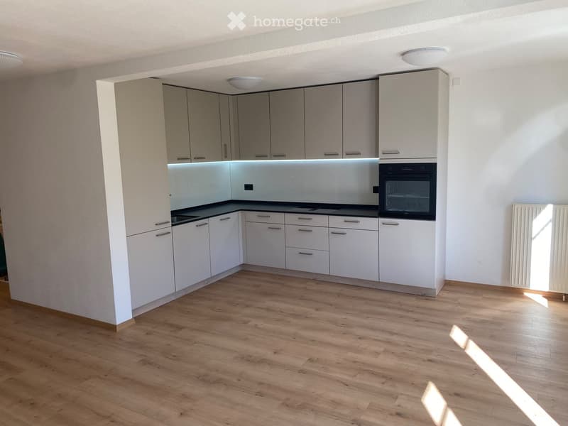 Modern kitchen with white cabinets, wooden flooring, and built-in oven.