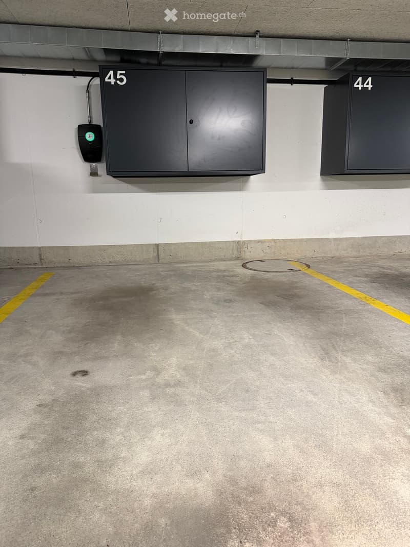 Underground parking garage with numbered storage cabinets and a charging station.