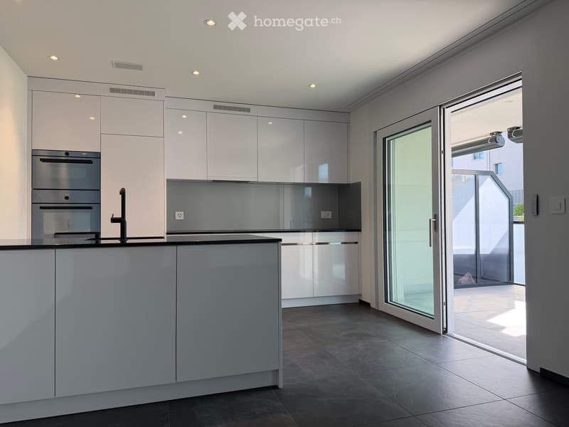 Modern kitchen with white cabinets, stainless steel oven, and a large sliding glass door leading to a balcony.