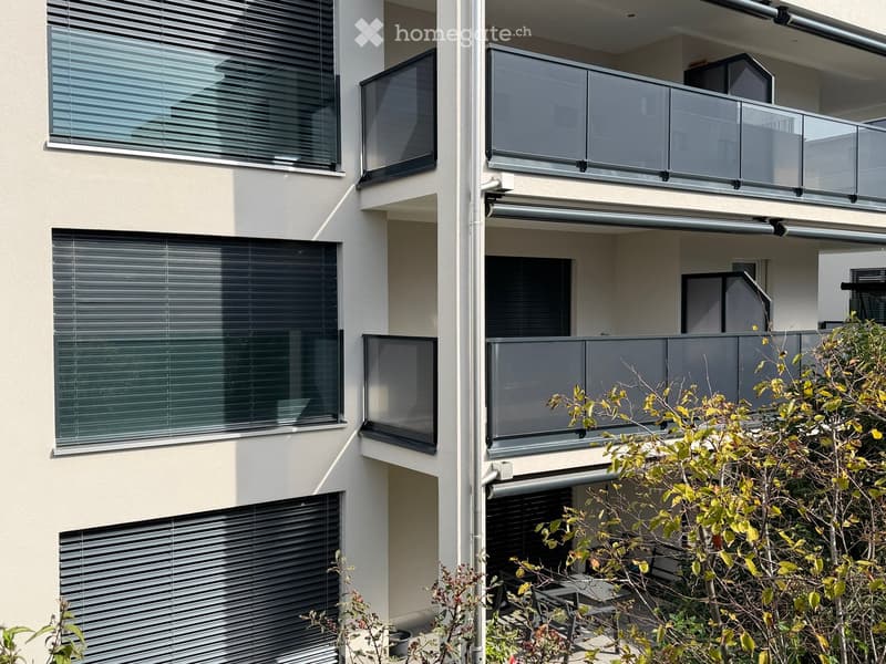 Modern multi-story building with large windows, glass balconies, and sleek blinds.