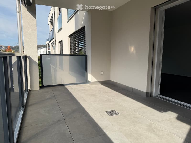 Modern balcony with tiled floor, glass railing, and sliding glass door leading to the interior.