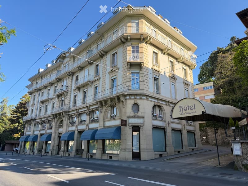 A multi-story building with classical architecture, featuring arched windows, balconies, and a sign reading "Hôtel Villa Toscana".