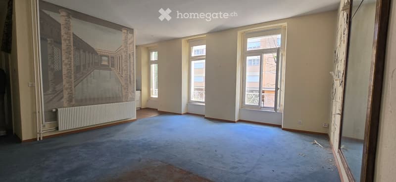 Empty room with beige walls, blue carpet, large windows, and a mural on one wall.