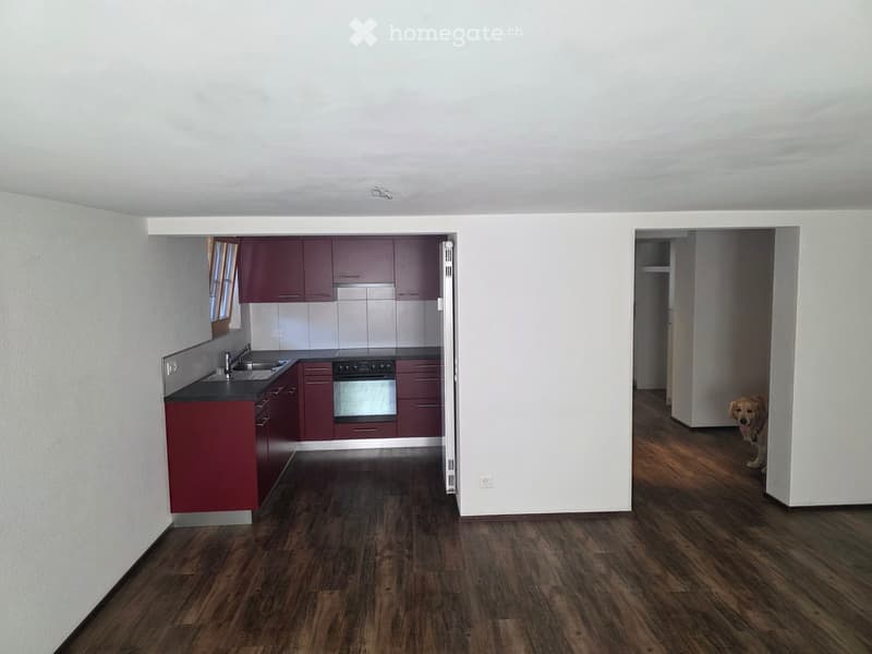 Modern kitchen with dark red cabinets, stainless steel sink, and oven. The room has wooden flooring and white walls.