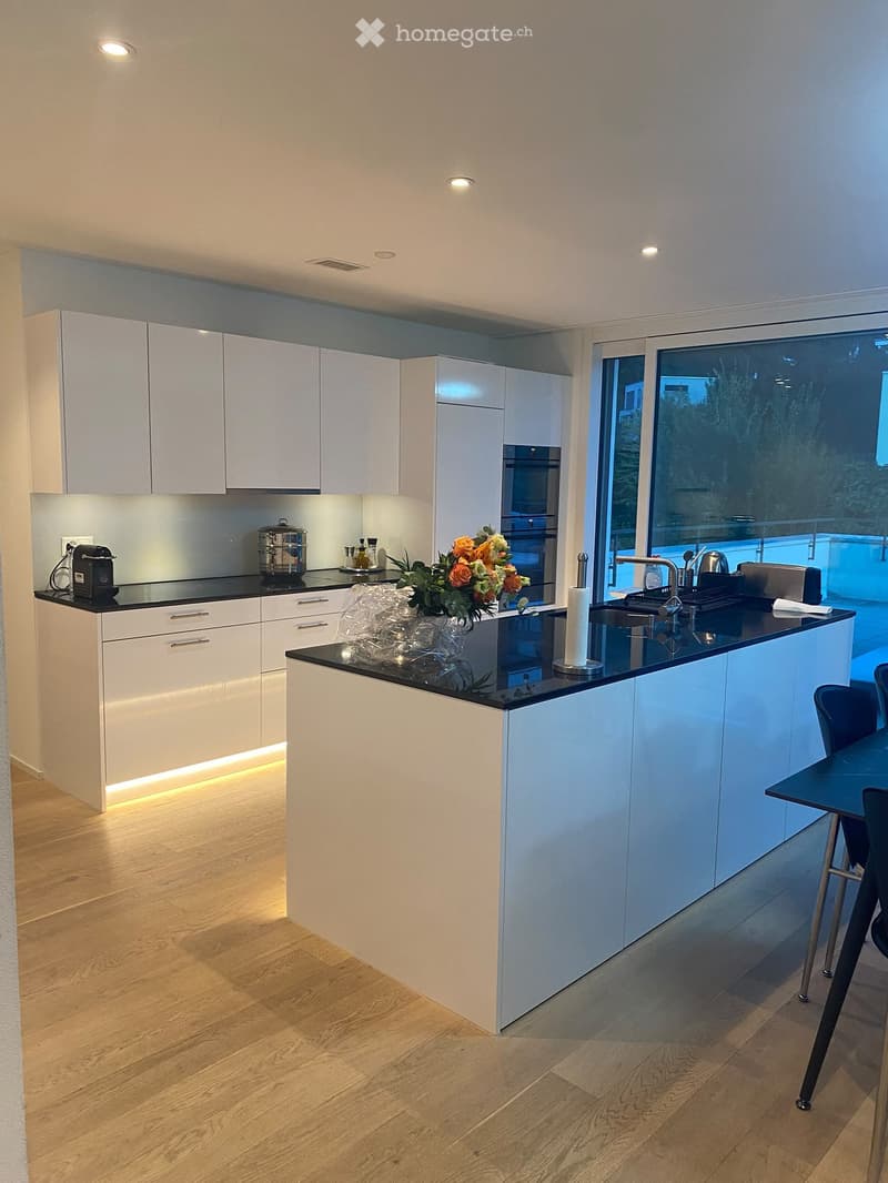Modern kitchen with white cabinets, black countertops, and a central island. Features include a sink, coffee maker, and a flower vase on the counter.