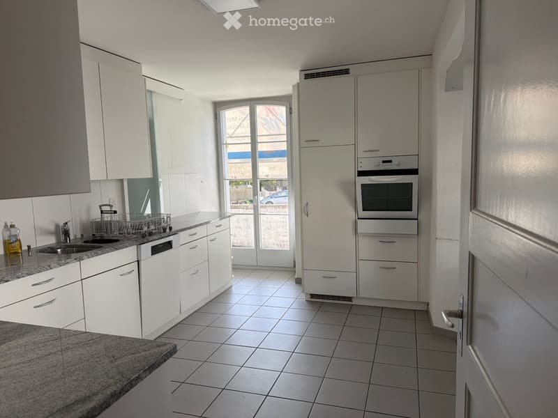 Modern kitchen with white cabinets, granite countertop, stainless steel sink, dishwasher, oven, refrigerator, and a bottle on the counter.