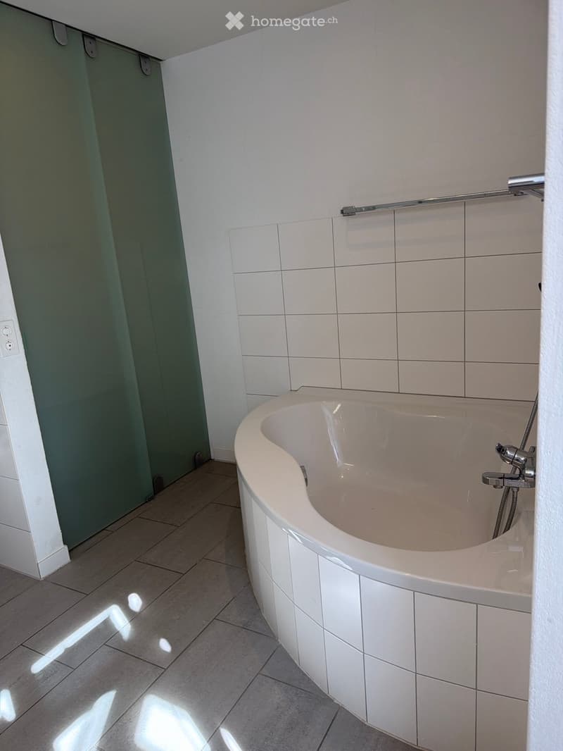 Modern bathroom with a white bathtub, tiled walls, and a shower curtain on the left side.