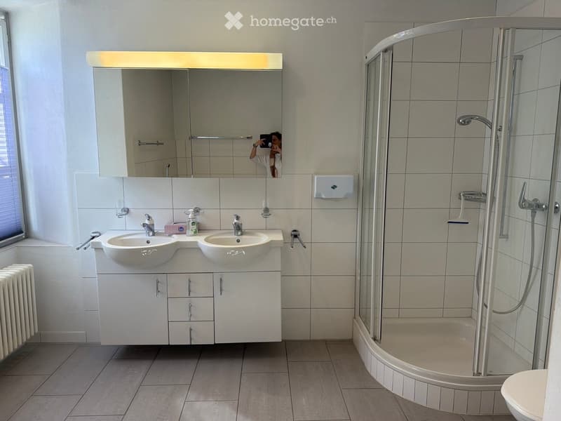 Modern bathroom with double sink, large mirror, glass-enclosed shower, and tiled walls and floor.