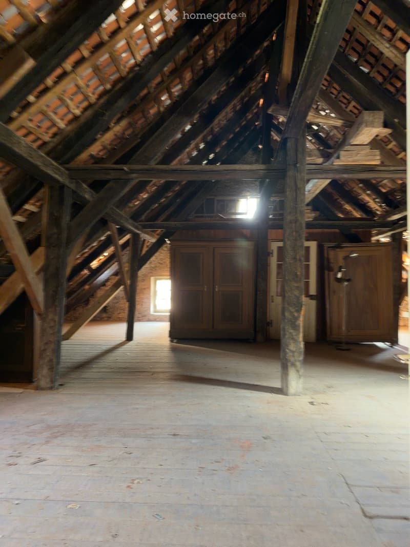 An attic space with exposed wooden beams and rafters, wooden floor, and a few wooden cabinets along the walls. The space is empty with no furniture or decorations.