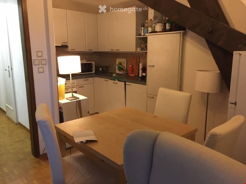 Modern kitchen with white cabinets, a dining table with chairs, a refrigerator, microwave, and a lamp on a side table.
