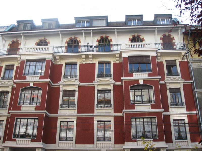 Multi-story residential building with red brick facade, white decorative trim, arched windows, and balconies with metal railings.