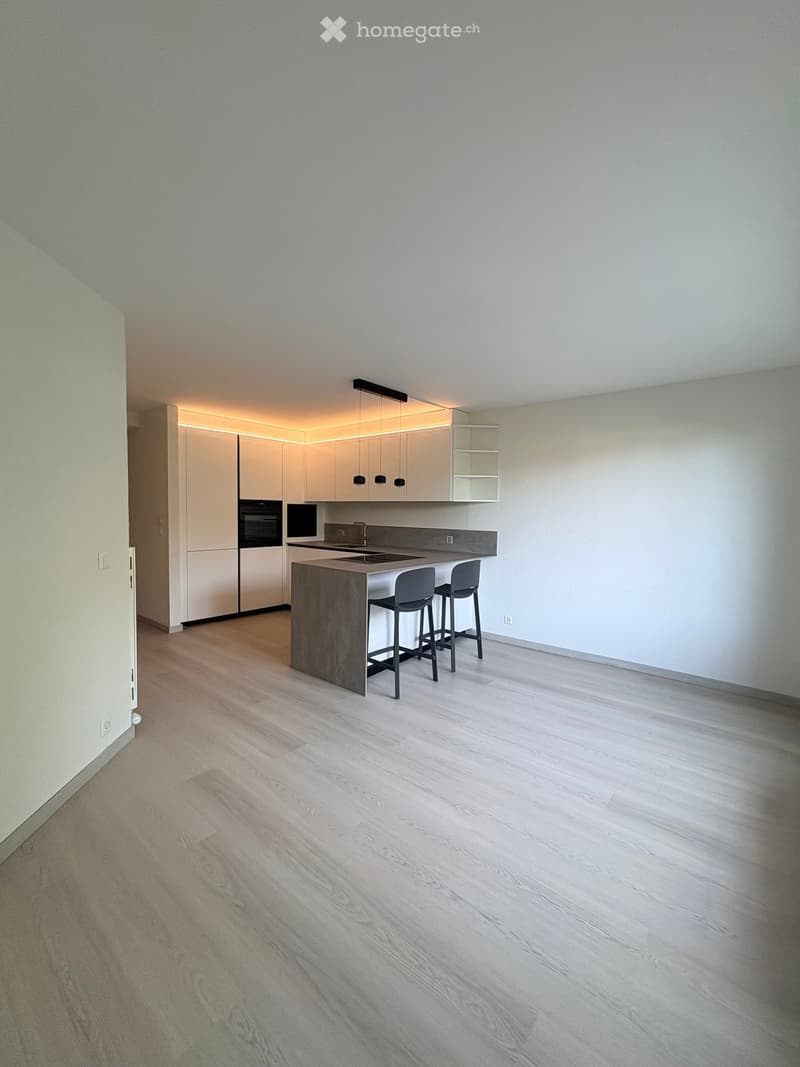 Modern kitchen with light-colored cabinetry, a central island with bar stools, and built-in appliances including an oven and sink.