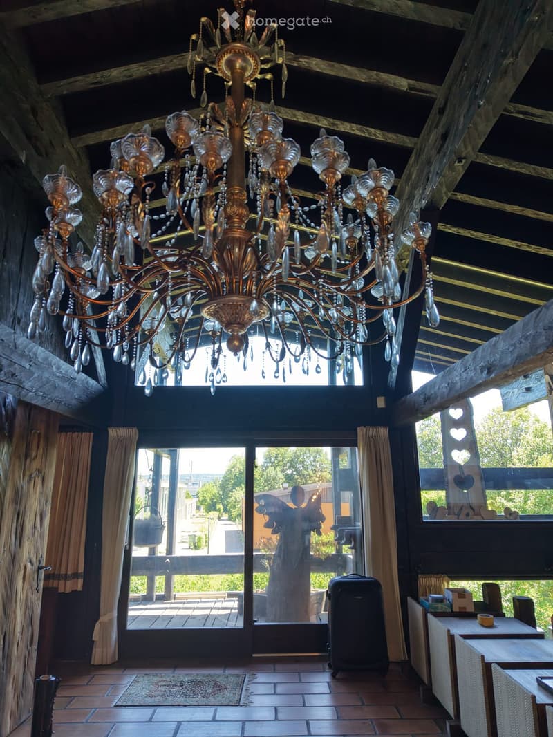 A room with a large, ornate chandelier, tiled floor, large windows with curtains, and a table with chairs.