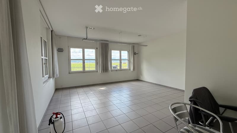 Empty room with white tiled floor, large windows with grey curtains, and a fire extinguisher in the corner.