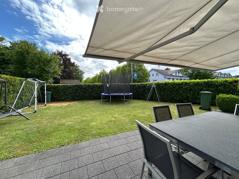 Well-maintained garden with a trampoline, swing set, and outdoor dining area under a pergola.