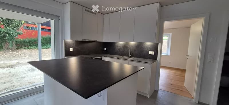Modern kitchen with white cabinets, black countertop, and a kitchen island. The space features a sink with a faucet and an open doorway leading to another room.