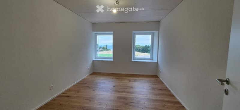 Empty room with wooden flooring, two windows offering a scenic view, and a single door.