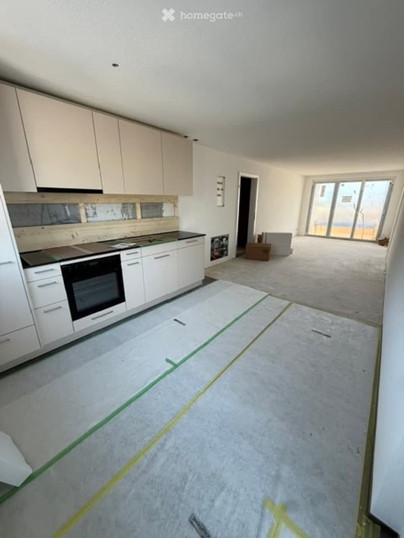 Empty kitchen area with white cabinets, a black oven, and a large window. The floor is covered with protective sheets, and there is a doorway leading to a balcony or terrace area.