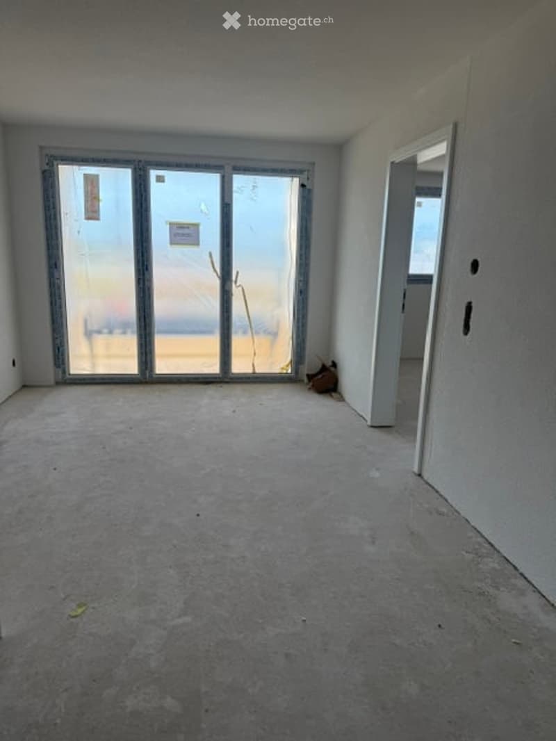 Empty room with bare walls, concrete floor, large glass sliding doors, and an open doorway leading to another space.