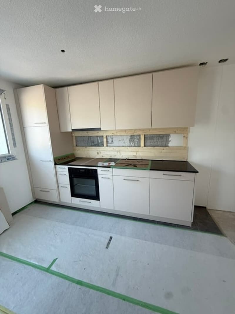 Modern kitchen with white cabinets, an oven, and a countertop. The floor is unfinished concrete, and the walls are painted white.