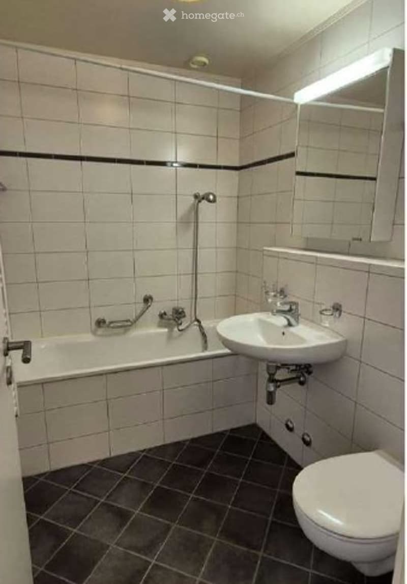 Modern bathroom with white tiled walls, black accent border, bathtub, sink, toilet, and mirror.