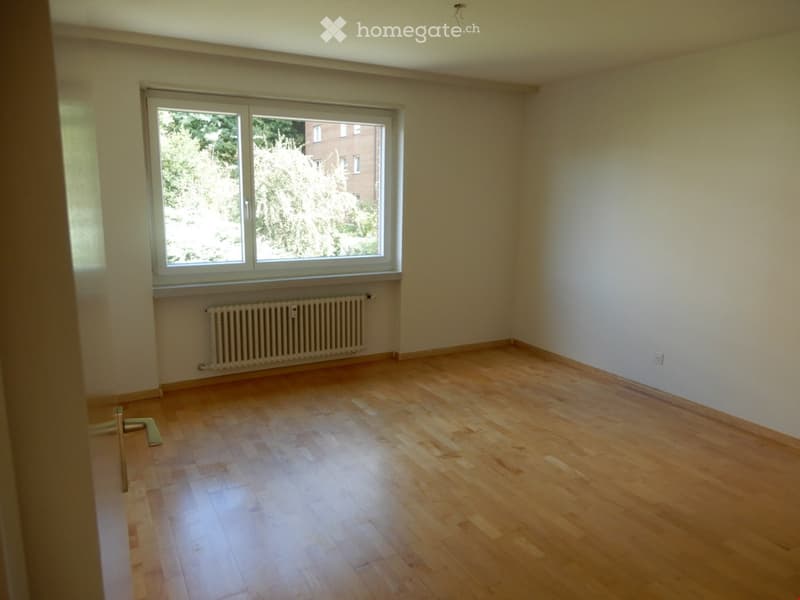 Empty room with wooden flooring, large window, radiator, and white walls.