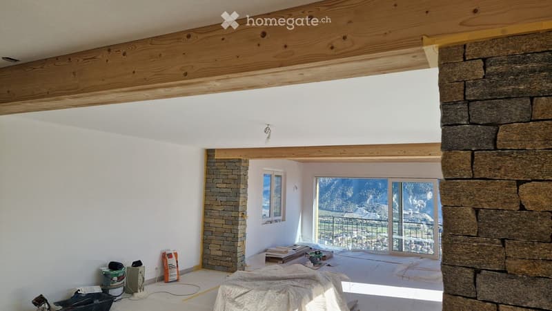 Empty room with exposed wooden beams, white walls, and a large window offering a scenic view. The floor is covered with protective sheets, and construction materials are visible near the window.