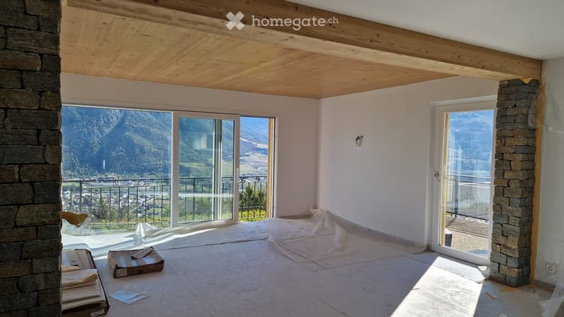 Empty room with large windows offering a scenic mountain view, wooden ceiling, and stone pillars.