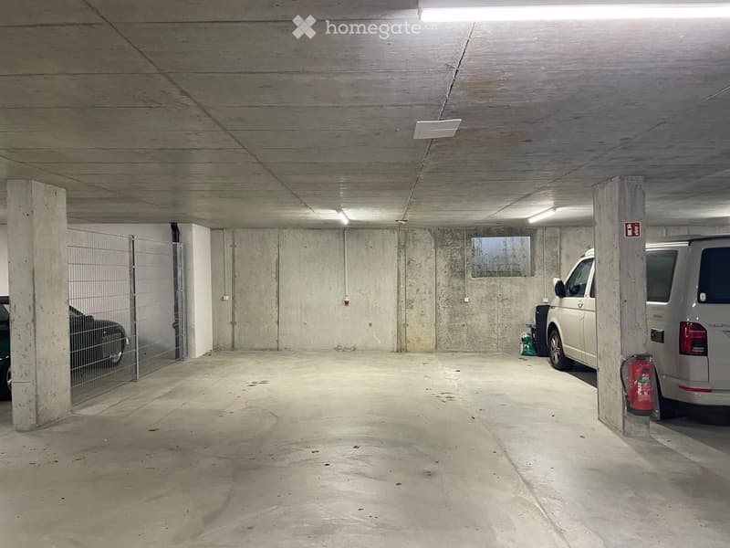 Underground parking area with concrete walls and pillars, a parked van, and a fire extinguisher.