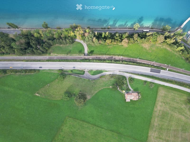 Aerial view of a rural area with a small house, green fields, roads, and a body of water in the background.