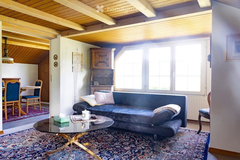 Living room with a blue sofa, glass coffee table, dining area with chairs and table, wooden cabinet, and large windows letting in natural light.