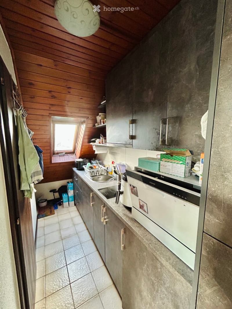 The kitchen features wooden walls, tiled flooring, and modern grey cabinets. A sink, fridge, oven, and dishwasher are visible, along with a window providing natural light.