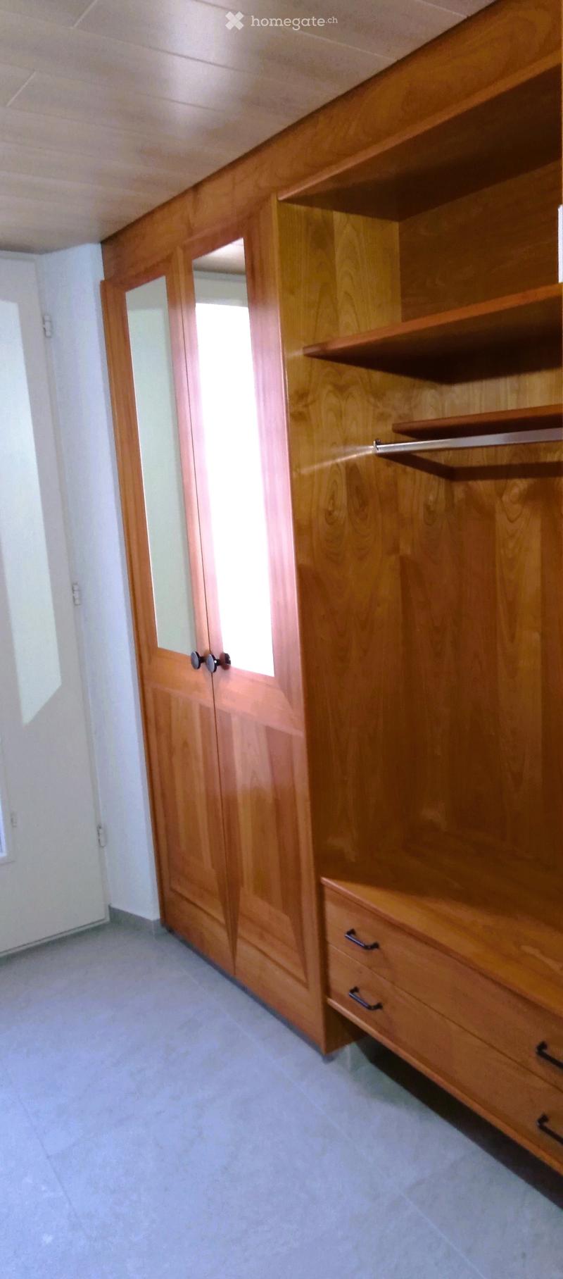 Empty room with wooden built-in closet featuring mirrored doors and open shelving, light-colored walls, and tiled floor.