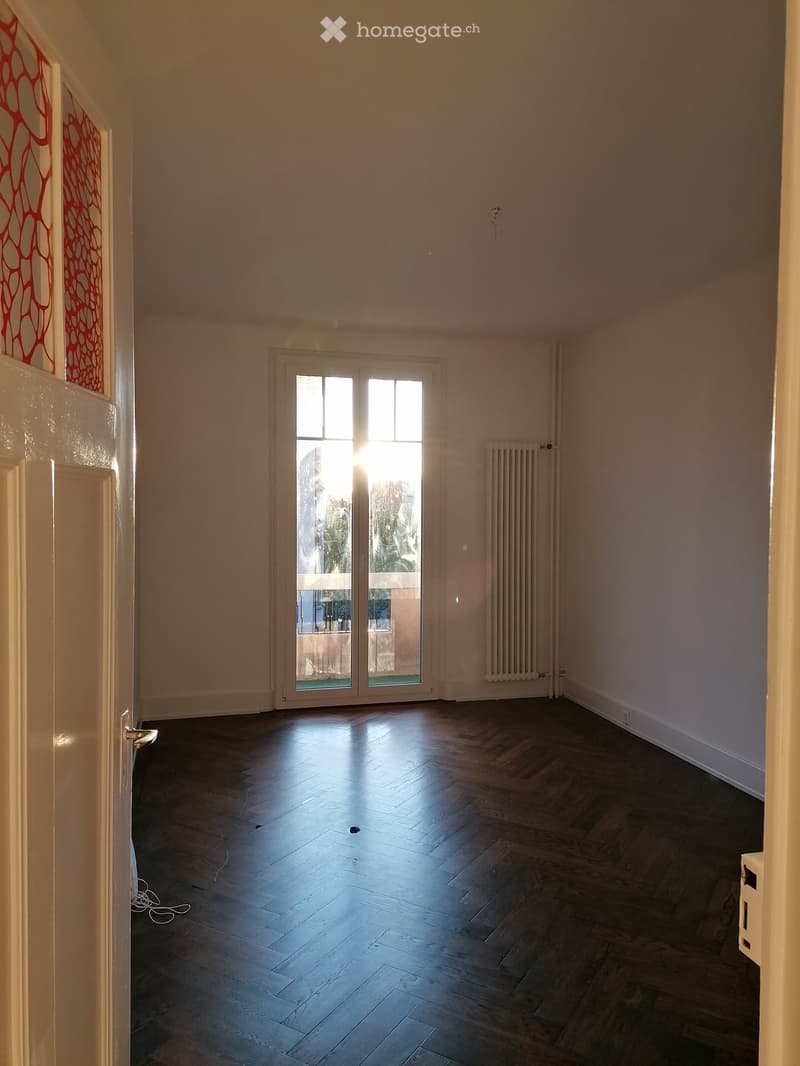 Empty room with wooden flooring, white walls, and a large glass door leading to a balcony.