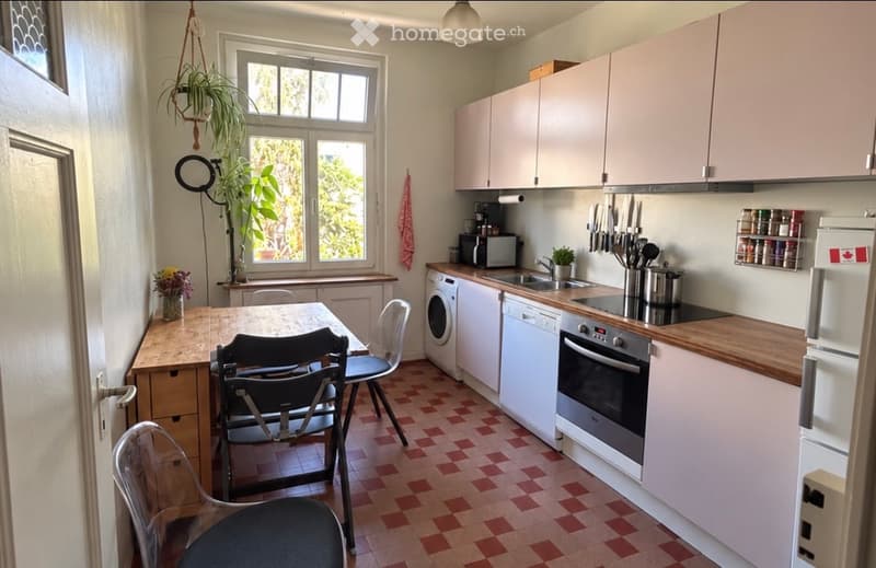 Bright kitchen with white cabinets, wooden countertops, and red-tiled floor. Includes a dining table with chairs, oven, refrigerator, microwave, sink, and various kitchen utensils.