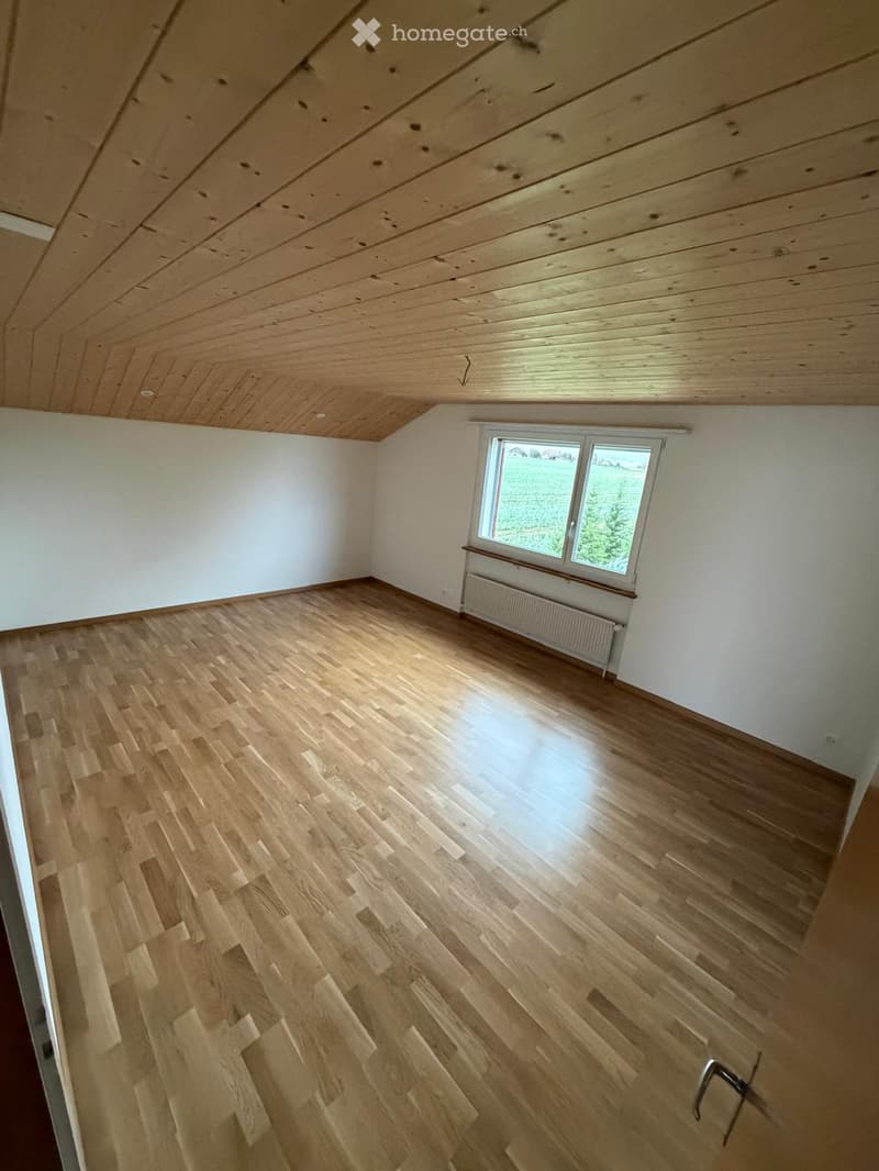 Empty room with wooden flooring, white walls, and a large window with a radiator below it.