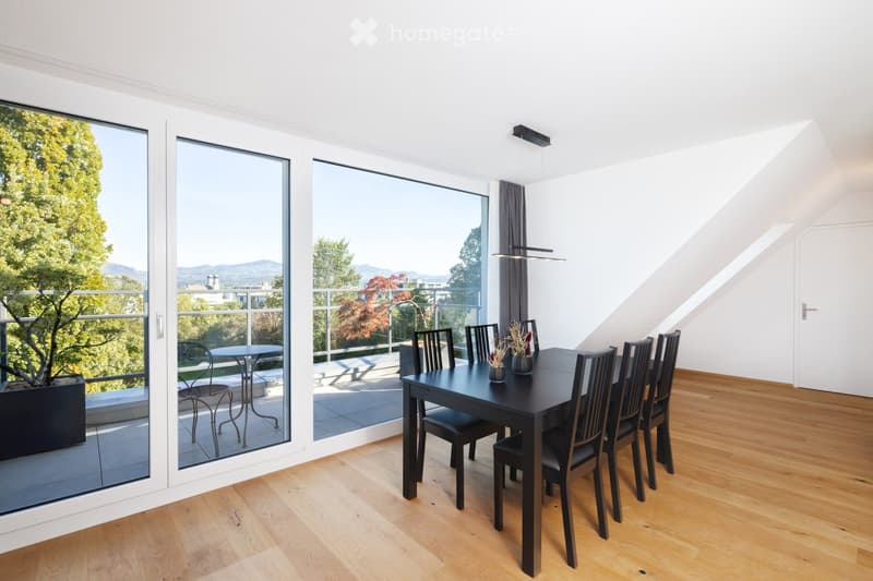 Modern dining room with wooden flooring, large windows offering a scenic view, a black dining table with six chairs, and a small table on the balcony.