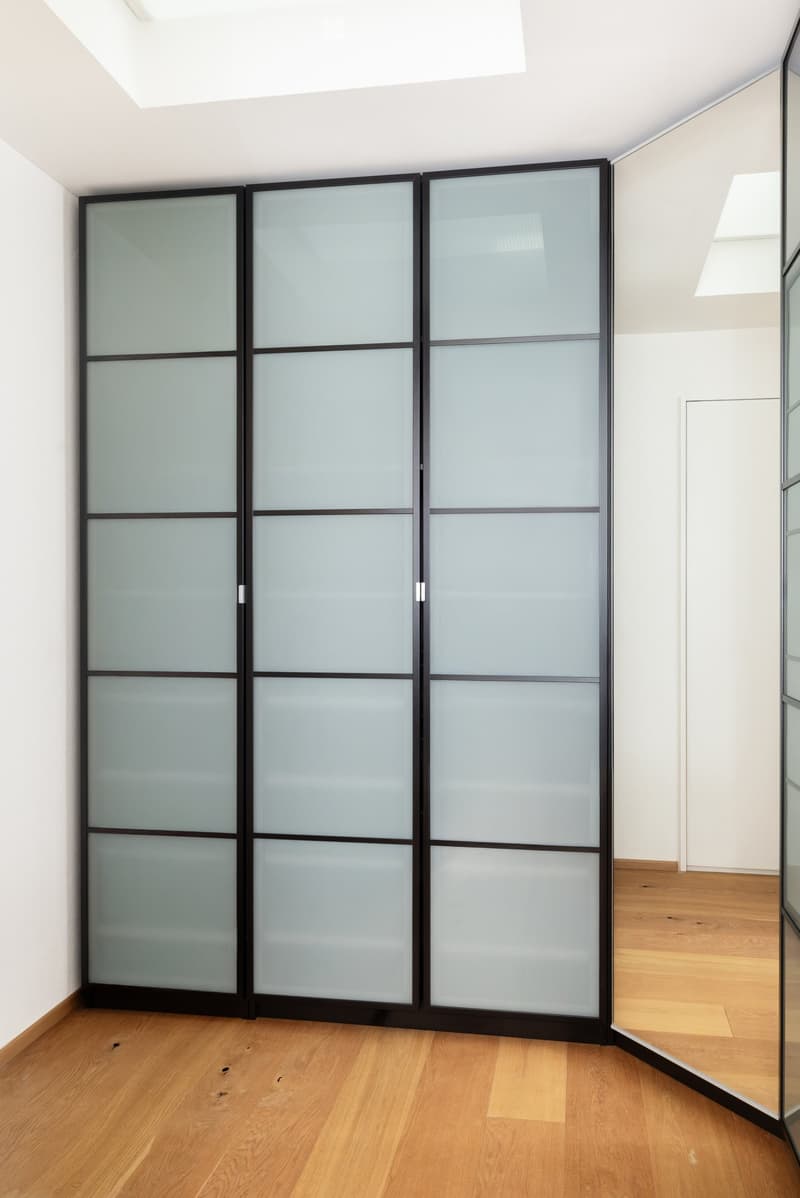 Empty room with light wooden flooring and white walls, featuring a large sliding glass partition with black frames.