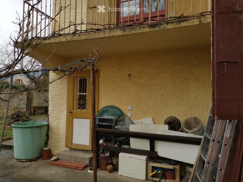 yellow exterior wall, entrance door, balcony with railings, large buckets, boxes, ladder