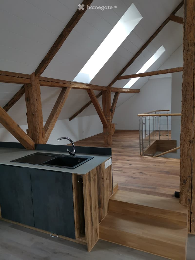 kitchen in an attic room with wooden beams, wooden floor, and a sink with a faucet