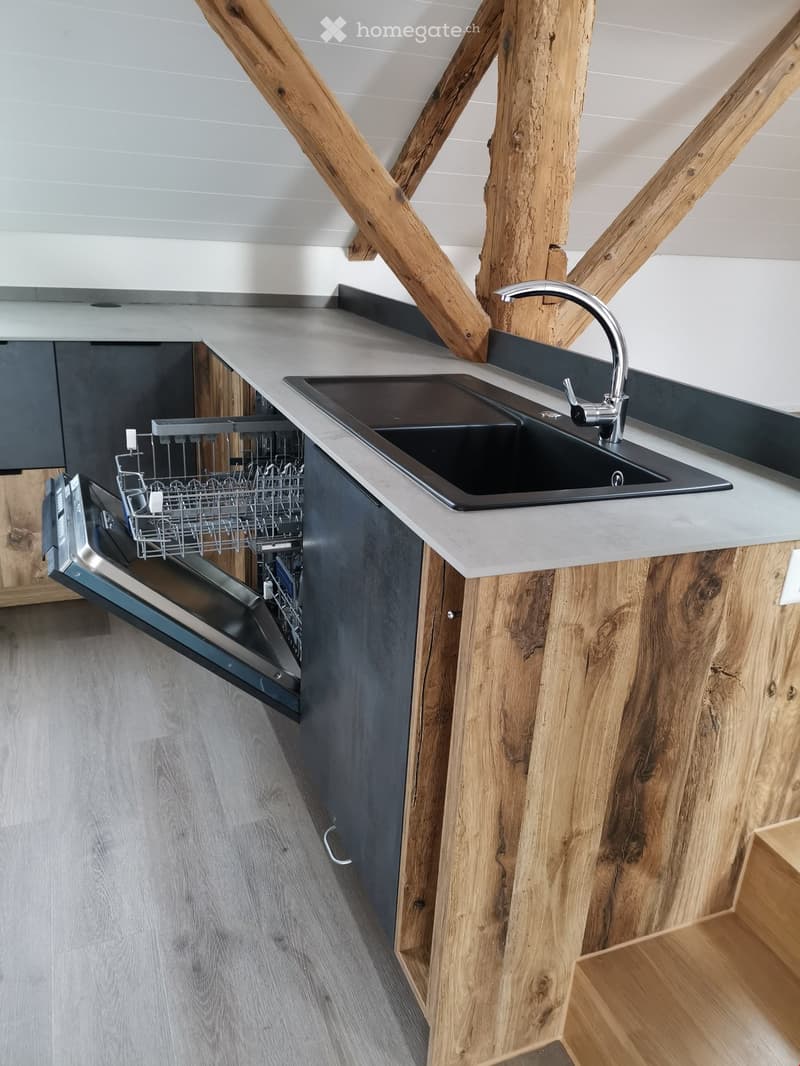 Modern kitchen with wooden walls and countertops, stainless steel sink, open dishwasher, wooden ceiling beams