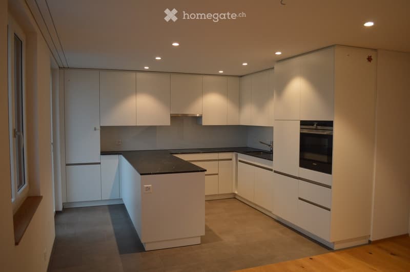 Modern kitchen with white cabinets, black countertop, and built-in oven. Features a sleek design with recessed lighting and a window on the left side.