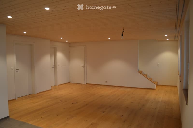 Empty room with wooden flooring, white walls, and recessed lighting. Features a staircase leading upwards and several doors.