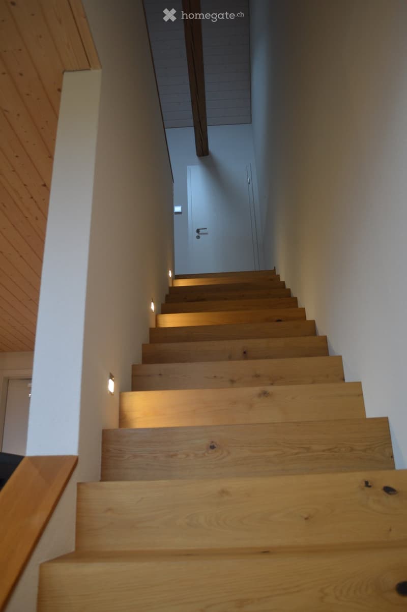 Wooden staircase with modern design, illuminated by wall-mounted lights, leading to a closed door at the end.